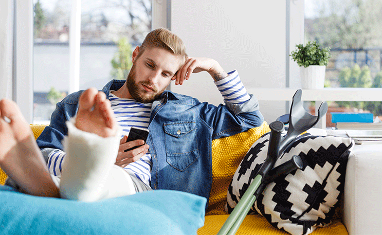 Un hombre mirando su teléfono con una lesión en su pierna sentado en el sofá