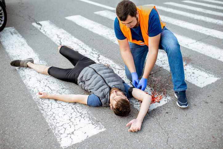 Un hombre esta tirado en el suelo de la carretera después de sufrir un atropello, aguantando su móvil y rodeado de cristales
