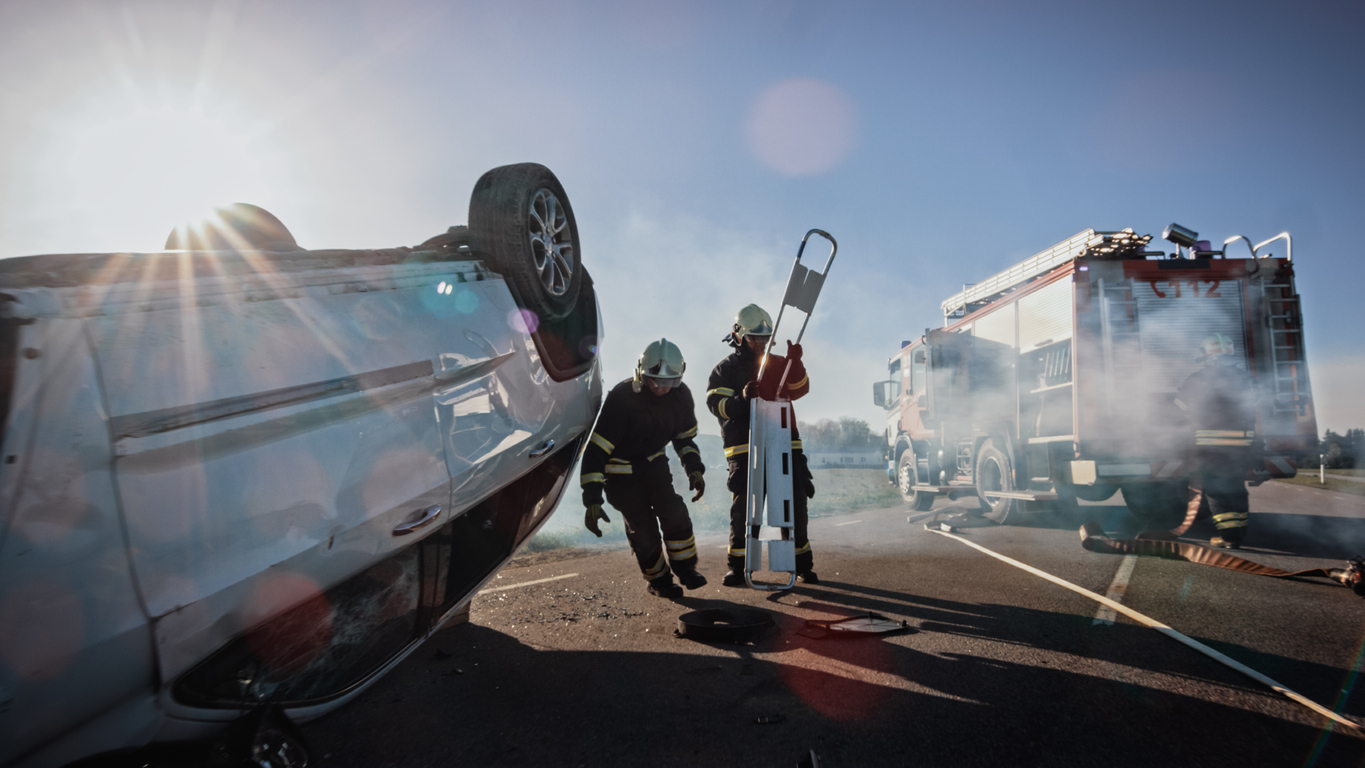 Dos bomberos intentando ayudar a salir de un auto chocado a la víctima del accidente que se quedó atrapada dentro del auto al volcar